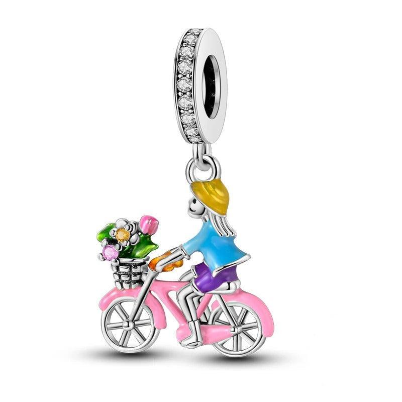 925 sterling silver charm showing a girl riding a pink bicycle with a flower basket, with a crystal-studded bail
